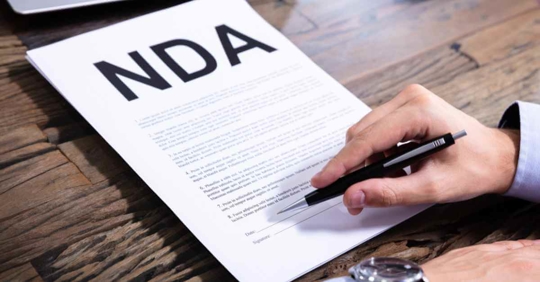A man signing a piece of paper that reads "NDA"